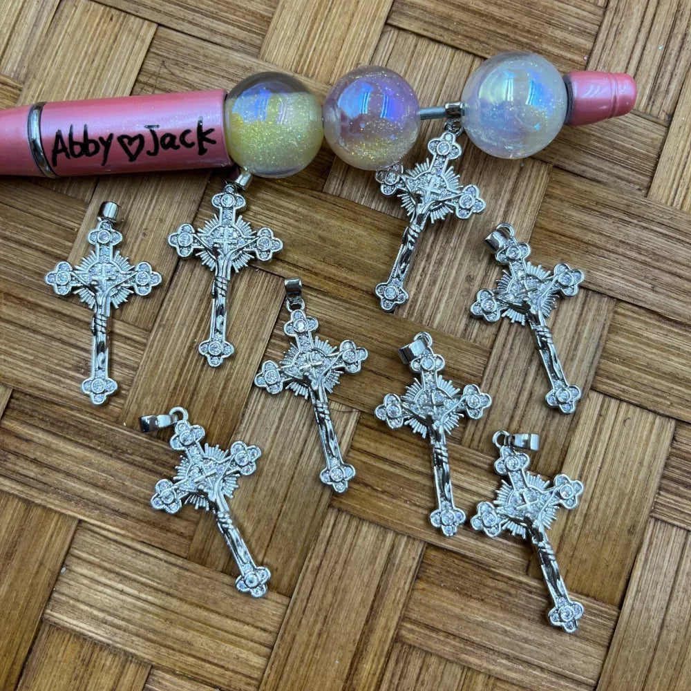 Silver ornate crucifix cross rhinestone charm pendant bail beads displayed on a woven surface next to a beadable pen, featuring detailed cross design with crystal rhinestone accents for DIY jewelry making.