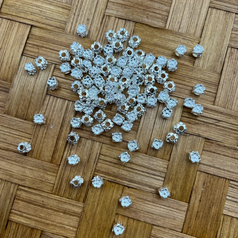Silver flower carved metal spacer beads with center hole scattered on a woven bamboo surface, used for beadable pens, keychains, and DIY jewelry making.