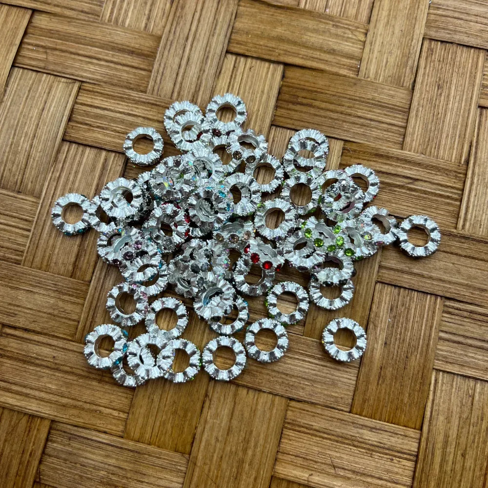 Pile of silver metal ring spacer beads with multicolor rhinestone crystal accents on woven bamboo surface, used for beadable pens, bracelets, and DIY jewelry making.