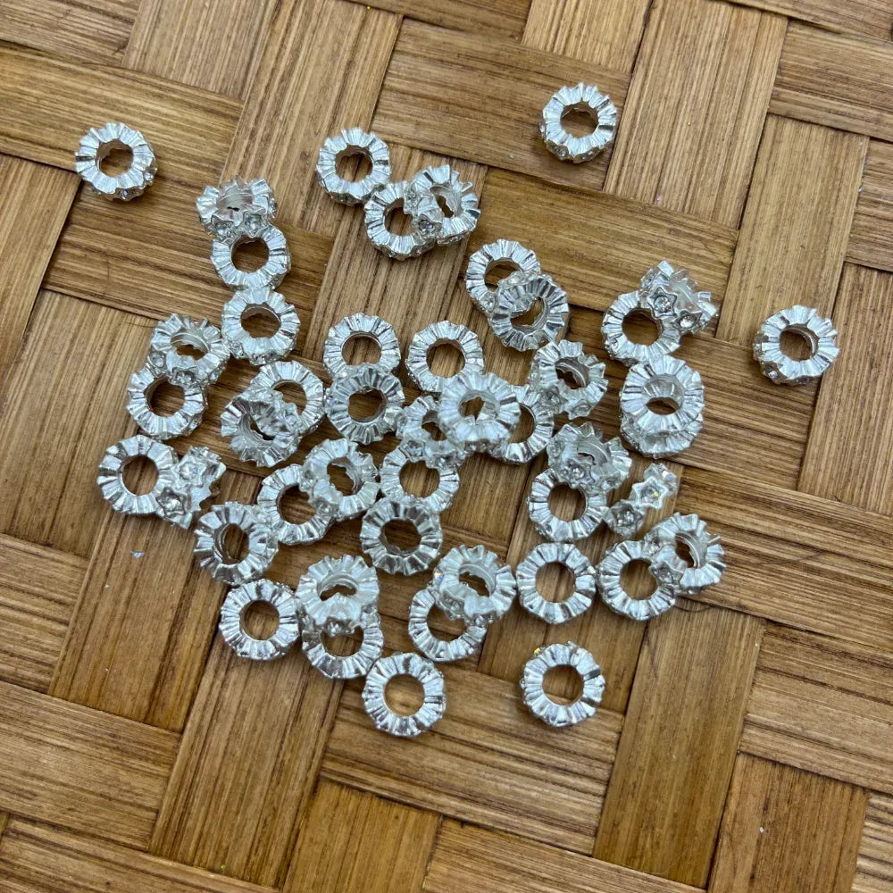 Silver rhinestone rondelle flower-shaped metal spacer beads with crystal accents scattered on a wicker surface, used for beadable pens, bracelets, and DIY jewelry making.