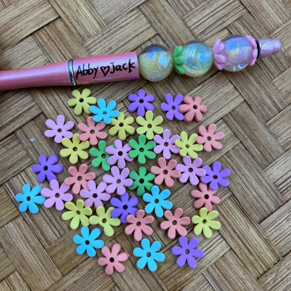 Assorted pastel daisy acrylic spacer beads displayed below a decorated pink beadable pen