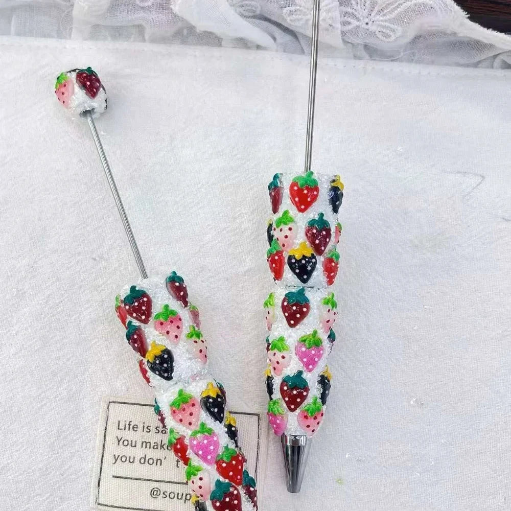 Close-up of two white glitter rhinestone pens decorated with red, pink, and black strawberry berry accents