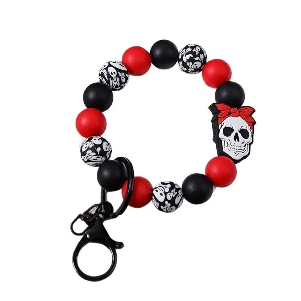 Red, black, and skull-patterned silicone beads bracelet keychain with a white skull wearing a red bow silicone bead focal piece and black lobster clasp.