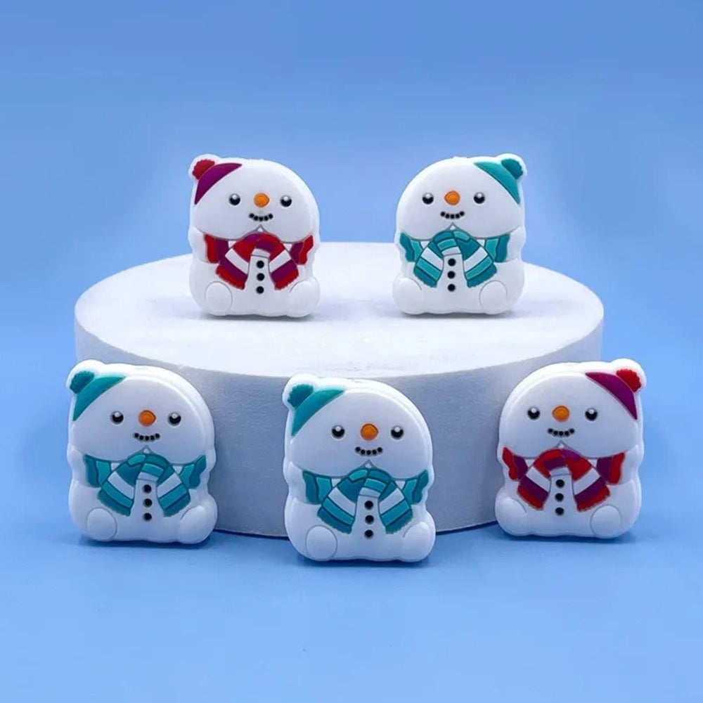 Five white silicone snowman focal beads wearing colorful striped scarves and knit hats in teal and red, displayed on a white pedestal with a blue background.