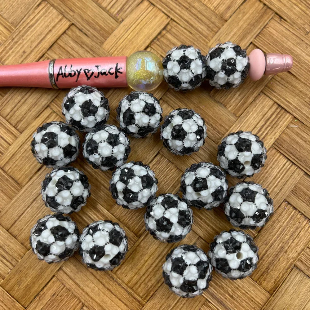 Black and white soccer ball patterned rhinestone beads displayed on a wicker surface next to a beadable pen, perfect for DIY jewelry making and beadable pens.