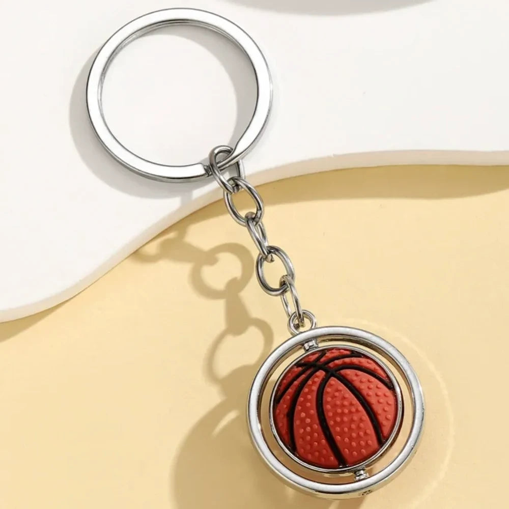 Set of 5 spinning sports ball keychain charms including soccer ball, basketball, football, baseball, and golf ball with silver metal rings on a cream background - Basketball