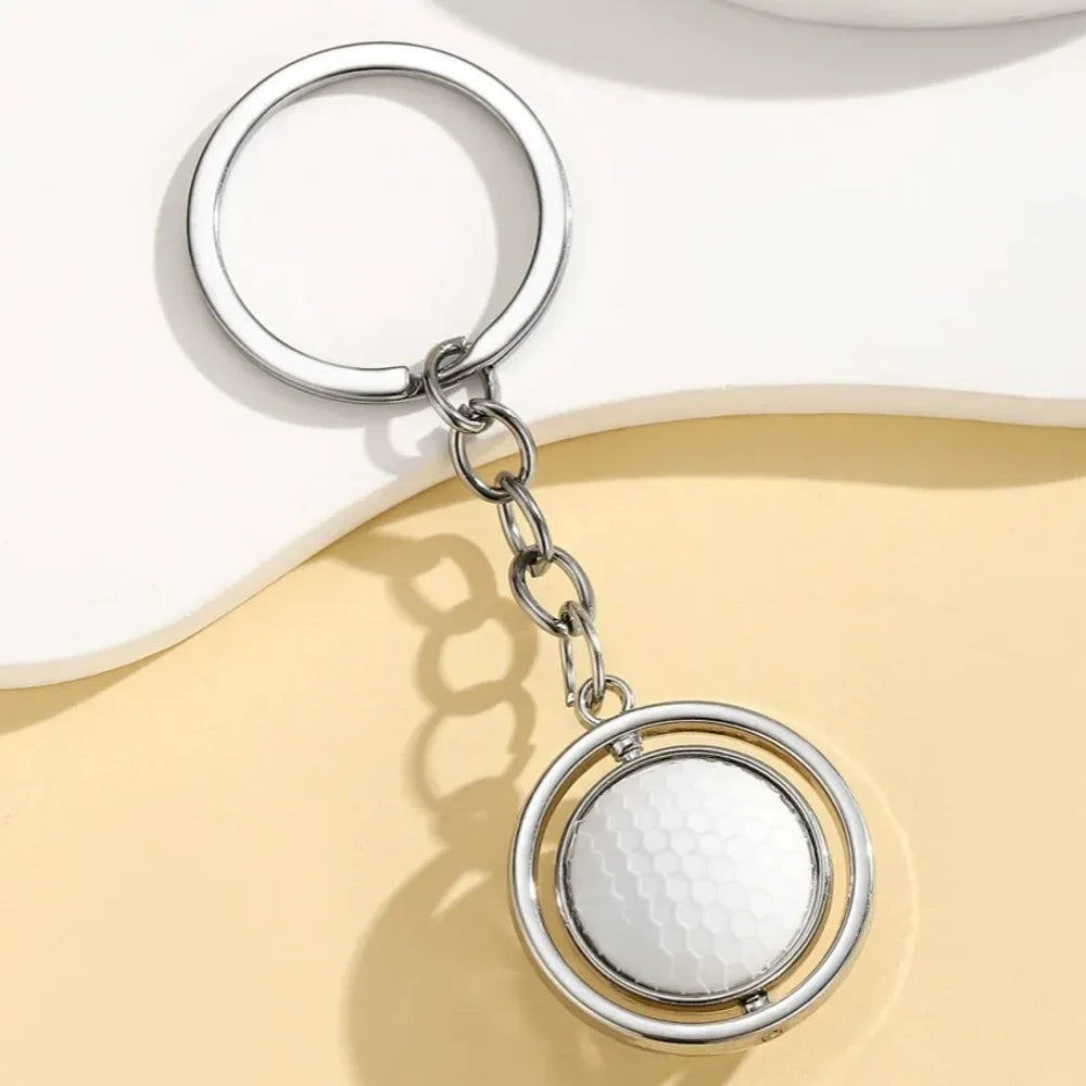 Set of 5 spinning sports ball keychain charms including soccer ball, basketball, football, baseball, and golf ball with silver metal rings on a cream background - Golf