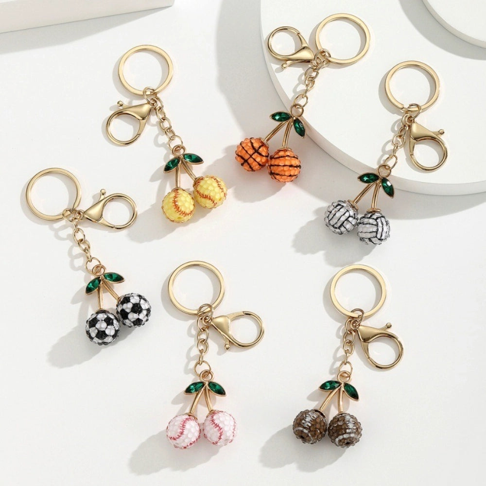 Set of 6 sports ball cherry charm keychains featuring soccer, basketball, baseball, softball, volleyball, and football designs with gold metal hardware and green crystal leaves on white background.