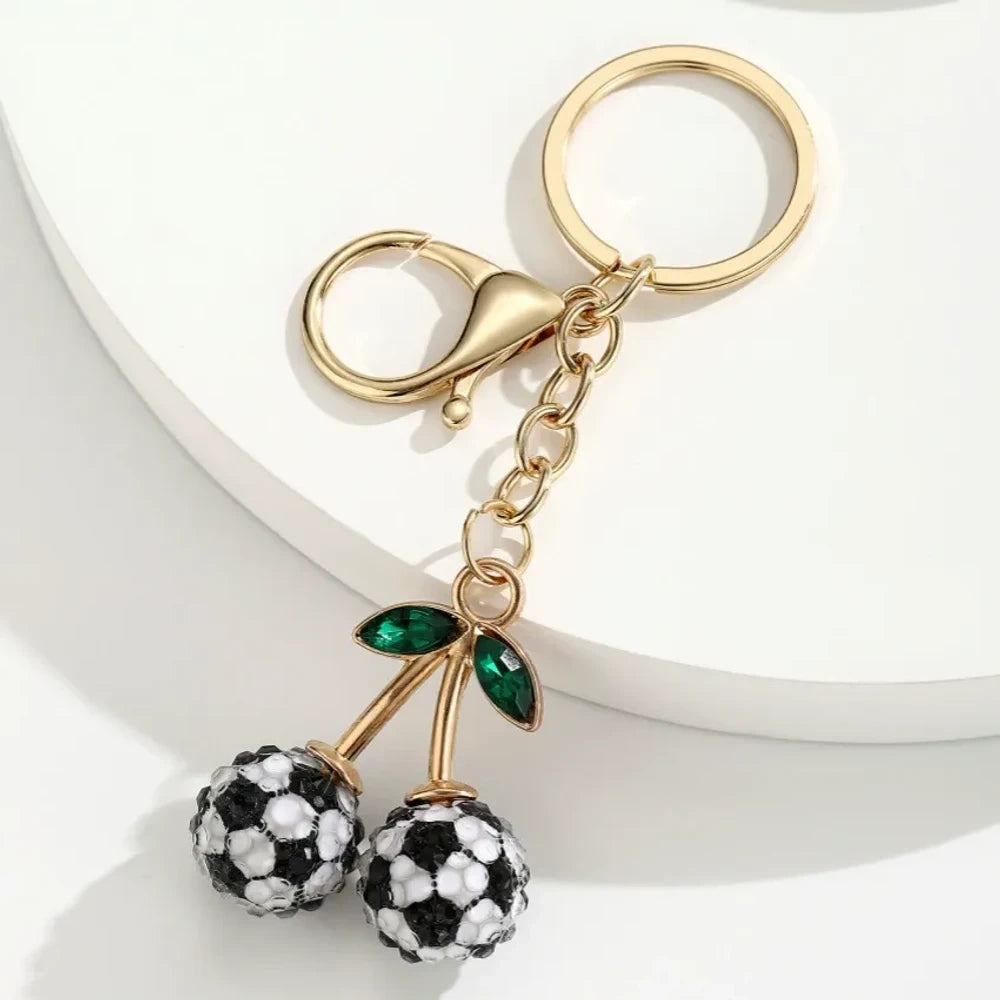 Set of 6 sports ball cherry charm keychains featuring soccer, basketball, baseball, softball, volleyball, and football designs with gold metal hardware and green crystal leaves on white background. - 1