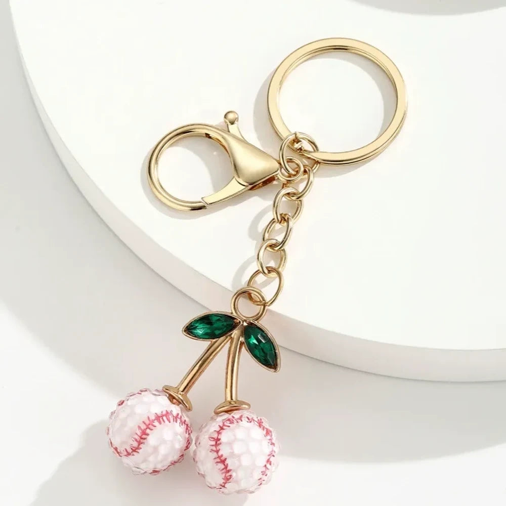 Set of 6 sports ball cherry charm keychains featuring soccer, basketball, baseball, softball, volleyball, and football designs with gold metal hardware and green crystal leaves on white background. - 2