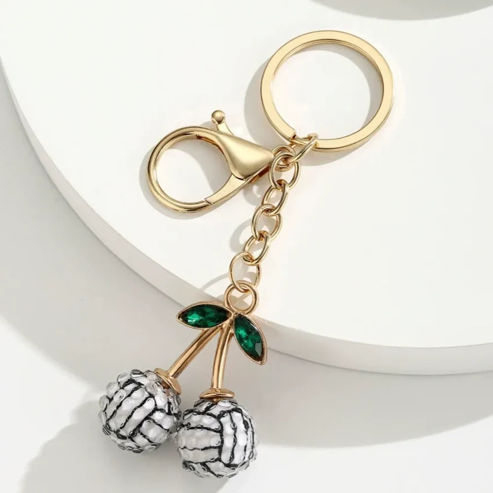 Set of 6 sports ball cherry charm keychains featuring soccer, basketball, baseball, softball, volleyball, and football designs with gold metal hardware and green crystal leaves on white background. - 3