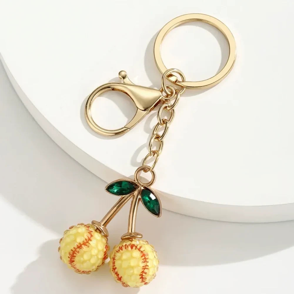 Set of 6 sports ball cherry charm keychains featuring soccer, basketball, baseball, softball, volleyball, and football designs with gold metal hardware and green crystal leaves on white background. - 4