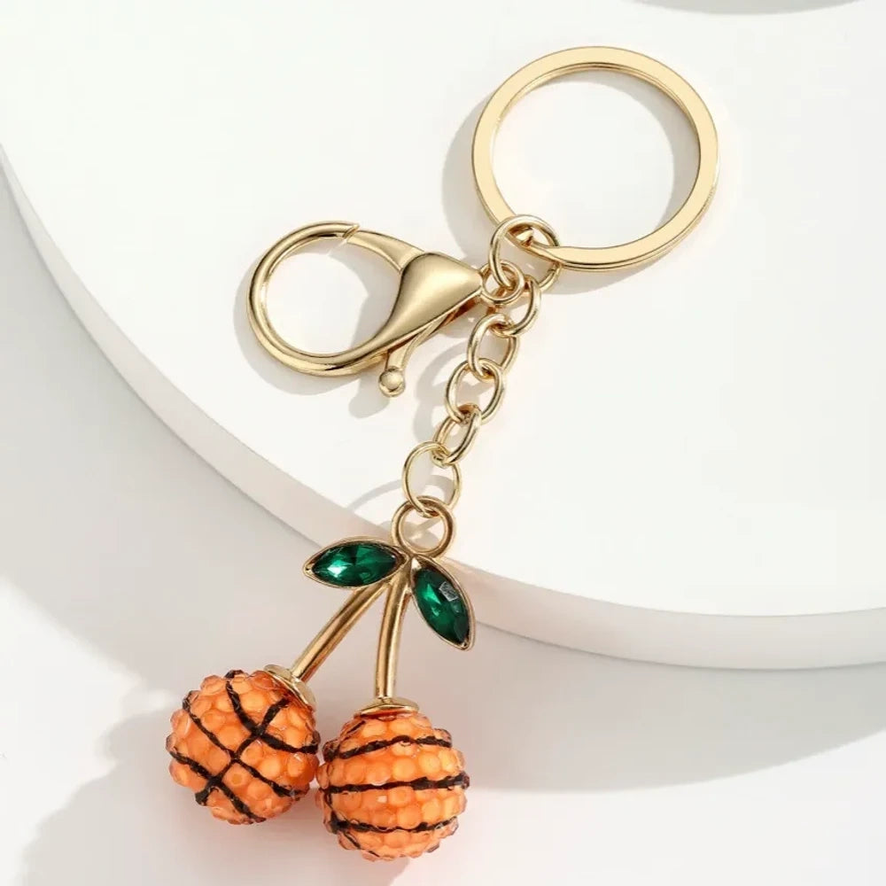 Set of 6 sports ball cherry charm keychains featuring soccer, basketball, baseball, softball, volleyball, and football designs with gold metal hardware and green crystal leaves on white background. - 5