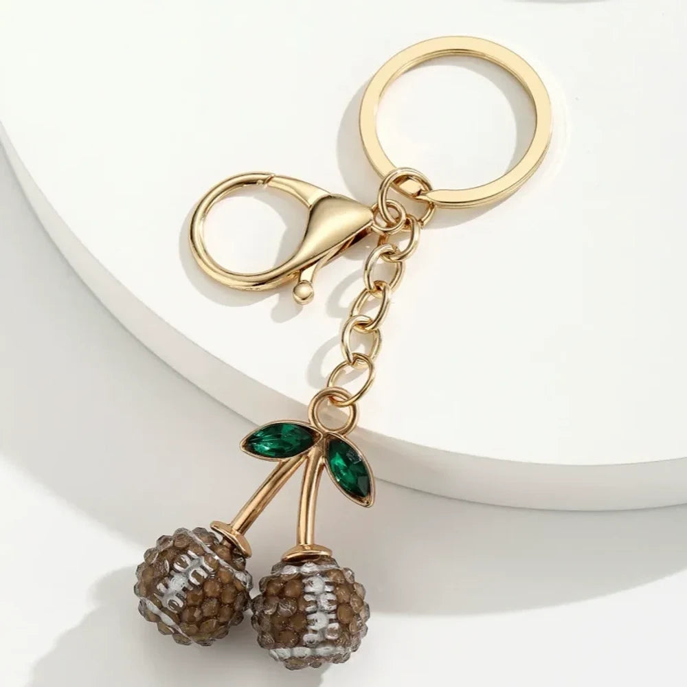 Set of 6 sports ball cherry charm keychains featuring soccer, basketball, baseball, softball, volleyball, and football designs with gold metal hardware and green crystal leaves on white background. - 6