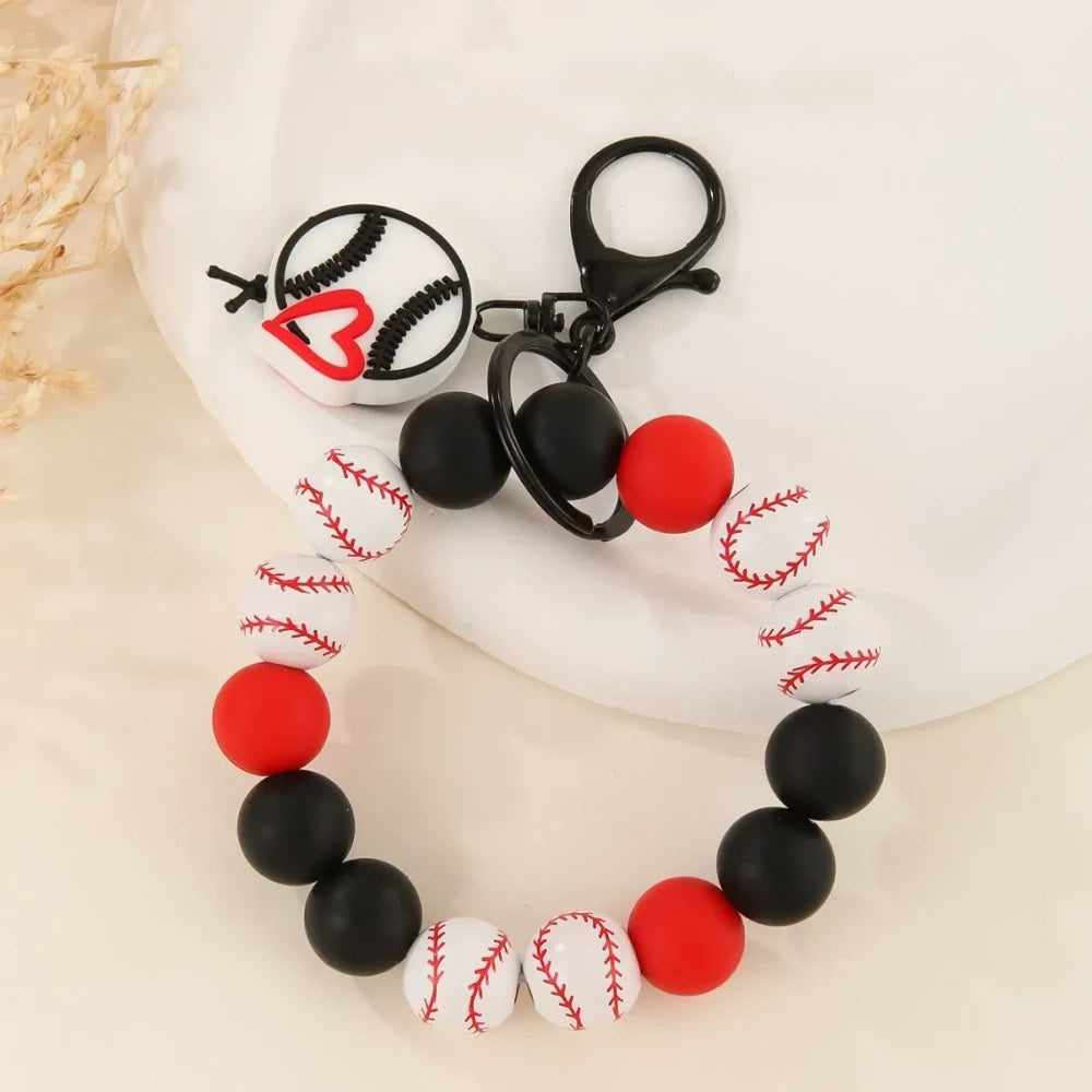 Assorted sports ball printed silicone beads and bracelet keychains featuring basketball, football, baseball, and volleyball designs with black hardware clasps on a white surface. - D