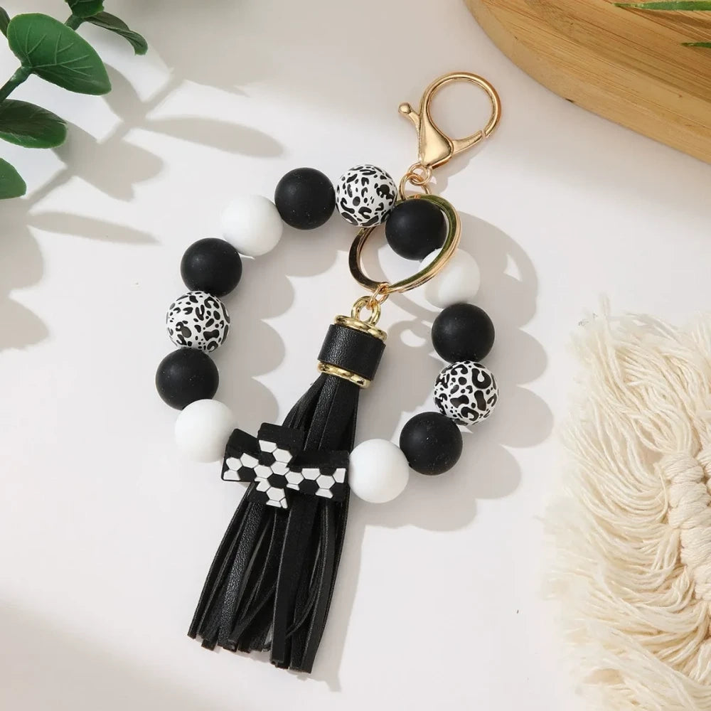 Set of 6 silicone bead stretch bracelet keychains featuring sports cross charms and leather tassels in assorted colors including red, blue, green, orange, black and white with leopard print beads and gold lobster clasp hardware. - Black