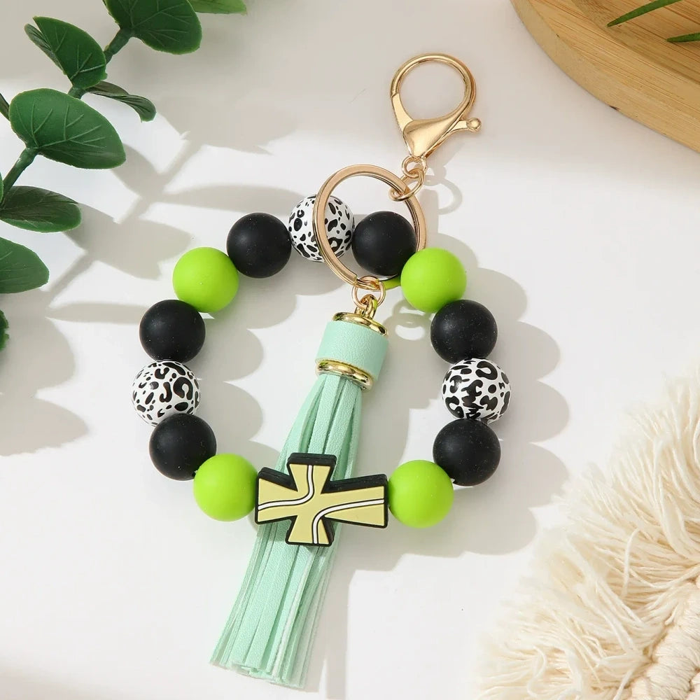 Set of 6 silicone bead stretch bracelet keychains featuring sports cross charms and leather tassels in assorted colors including red, blue, green, orange, black and white with leopard print beads and gold lobster clasp hardware. - Green