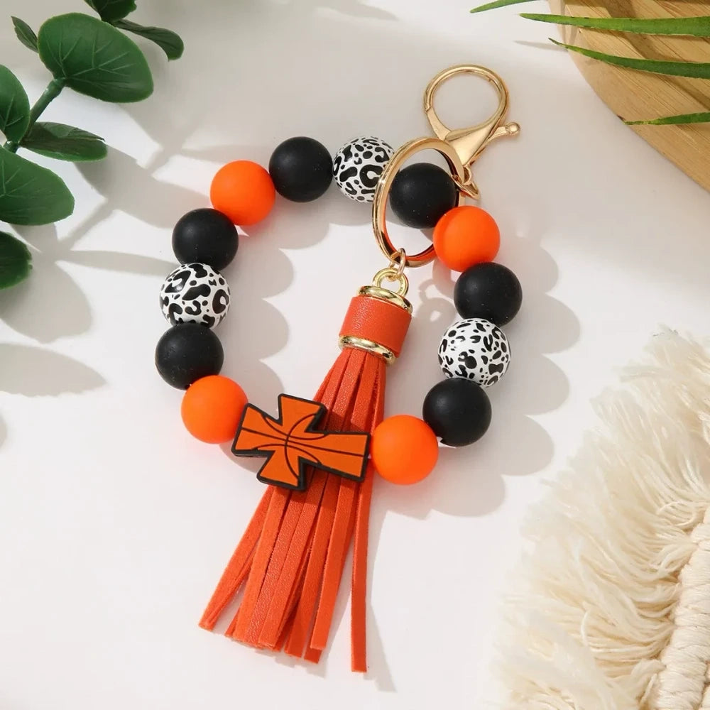 Set of 6 silicone bead stretch bracelet keychains featuring sports cross charms and leather tassels in assorted colors including red, blue, green, orange, black and white with leopard print beads and gold lobster clasp hardware. - Orange