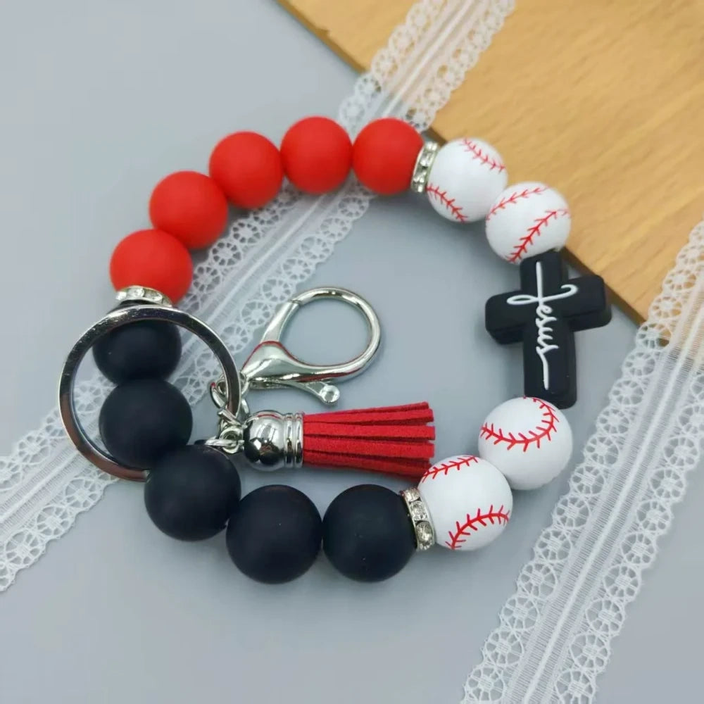 Assorted sports print silicone beads in basketball, football, baseball, soccer, and volleyball designs with matching solid color beads, shown on completed beaded bracelet keychains with cross charms and tassels. - Baseball