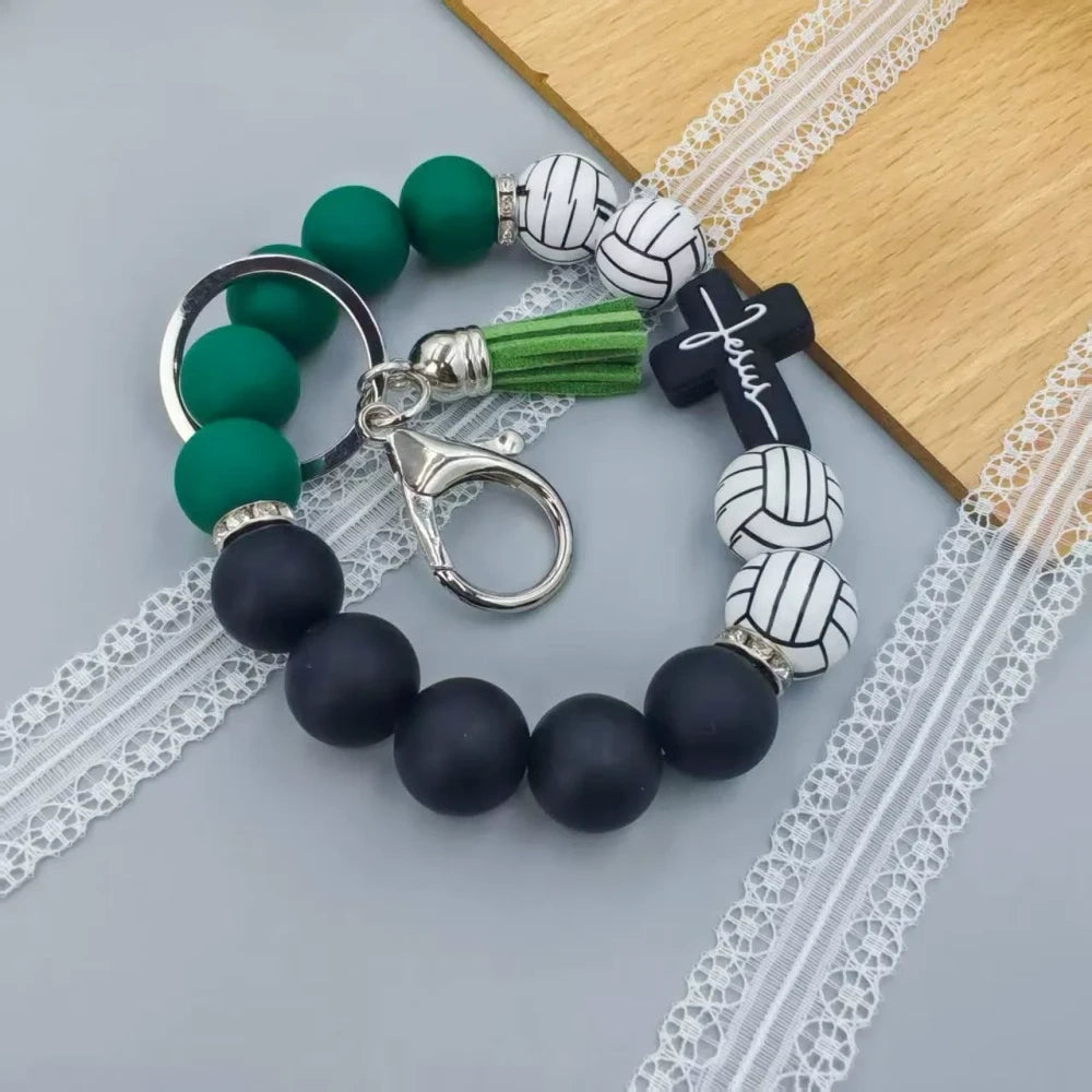 Assorted sports print silicone beads in basketball, football, baseball, soccer, and volleyball designs with matching solid color beads, shown on completed beaded bracelet keychains with cross charms and tassels. - Volleyball