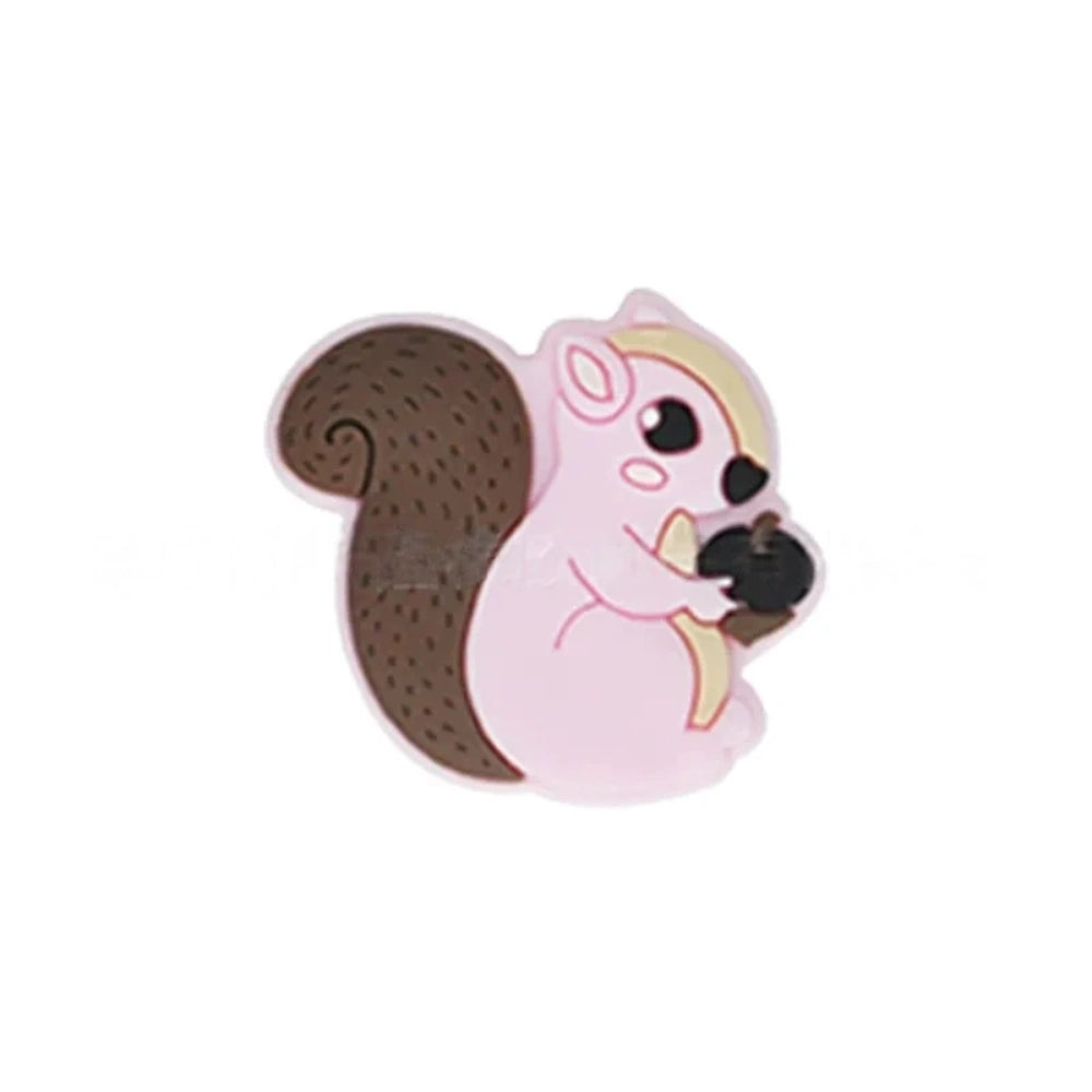 Six cute cartoon squirrel silicone focal beads holding acorns in brown, yellow, grey, dark pink, light pink, and blue colors arranged on a miniature white bench. - Light Pink