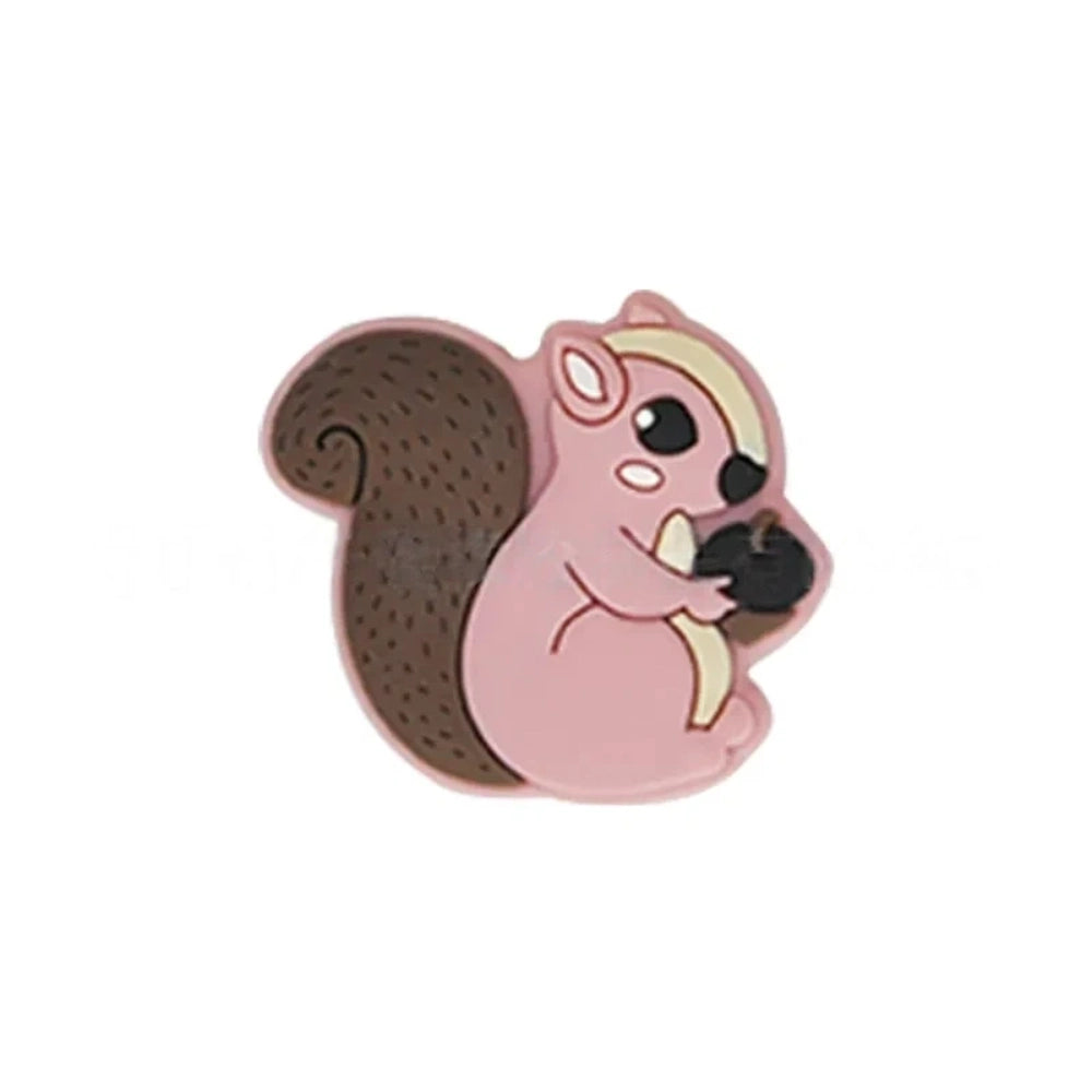 Six cute cartoon squirrel silicone focal beads holding acorns in brown, yellow, grey, dark pink, light pink, and blue colors arranged on a miniature white bench. - Pink