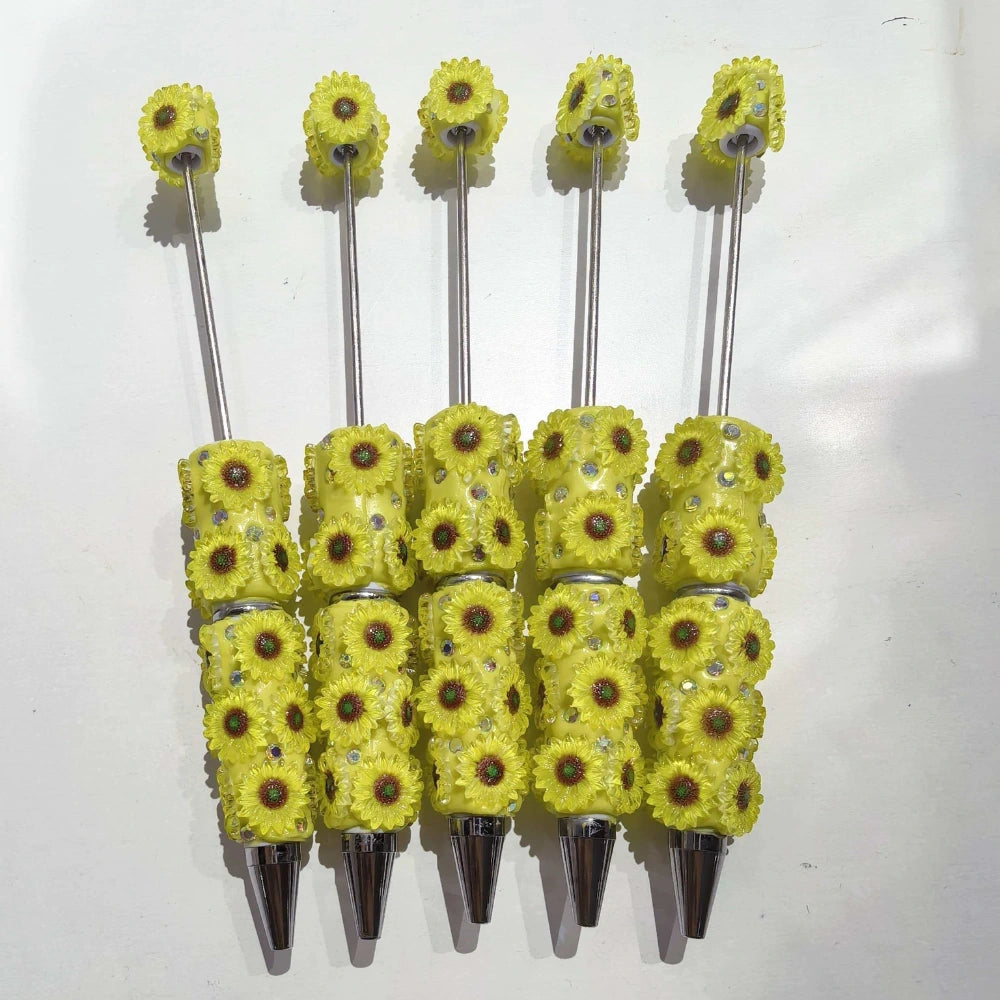 Five yellow sunflower clay beadable pens with rhinestone embellishments and silver metallic tips, arranged side by side on white background.