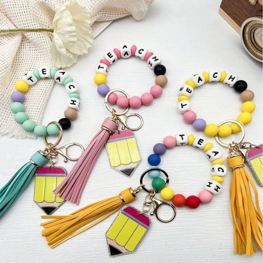Colorful TEACH letter printed silicone bead bracelet keychains with pencil charms and tassel accents in mint, pink, rainbow, and yellow color combinations