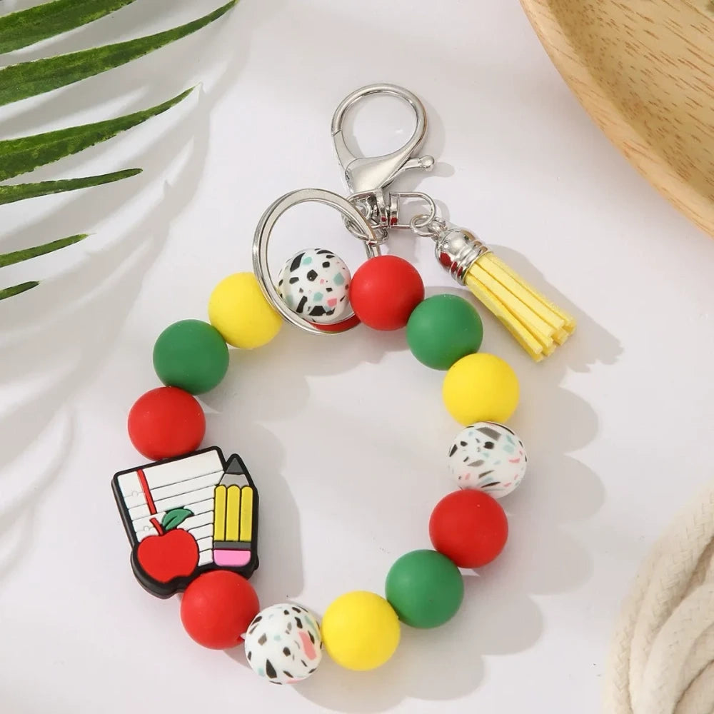 Eight teacher-themed silicone bead keychains featuring apple and pencil charms, colorful red, green, yellow, and mint beads with tassels, labeled Best Teacher Ever and A+ Teacher. - 1