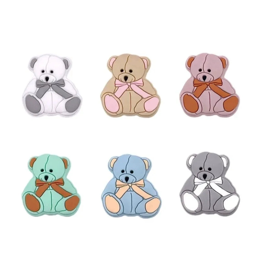 Six teddy bear silicone focal beads in white, tan, pink, mint, blue, and gray, each with a bow tie accent, displayed on a white background for DIY craft projects.
