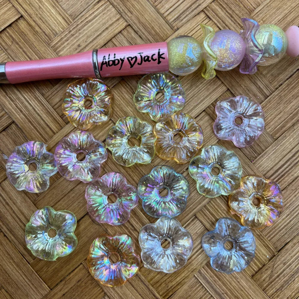 Translucent pastel iridescent flower acrylic spacer beads with center holes displayed beside a pink beadable pen