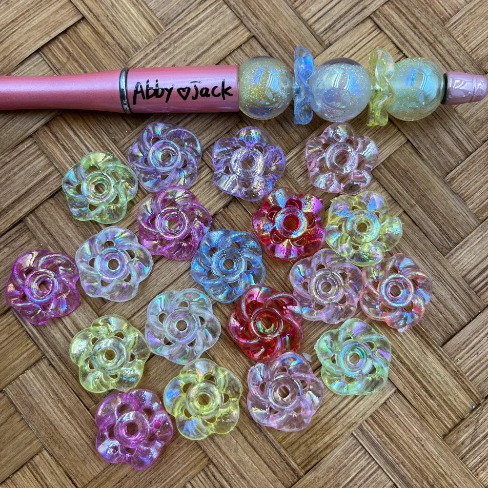 Mixed iridescent flower acrylic spacer beads in translucent pink, purple, blue, yellow, green, and red beside a beadable pen