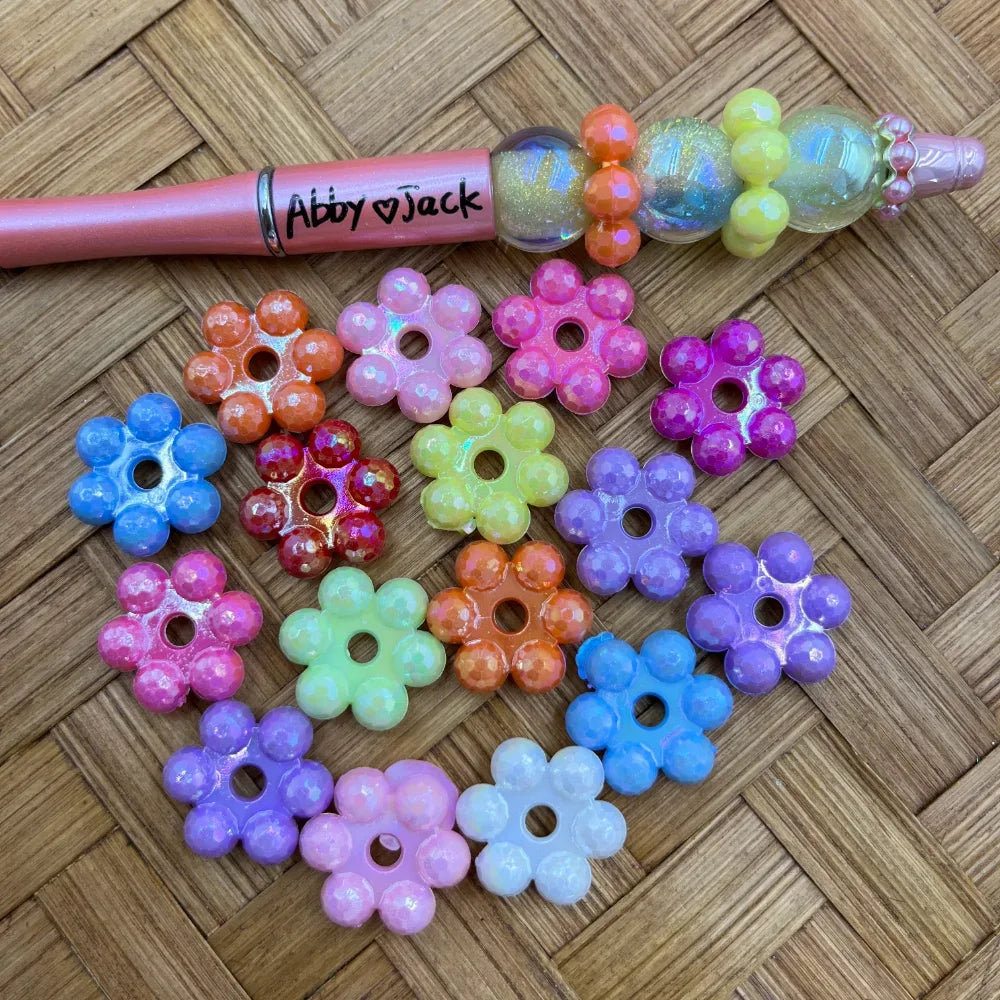 Assorted pastel iridescent flower acrylic spacer beads shown with a decorated beadable pen